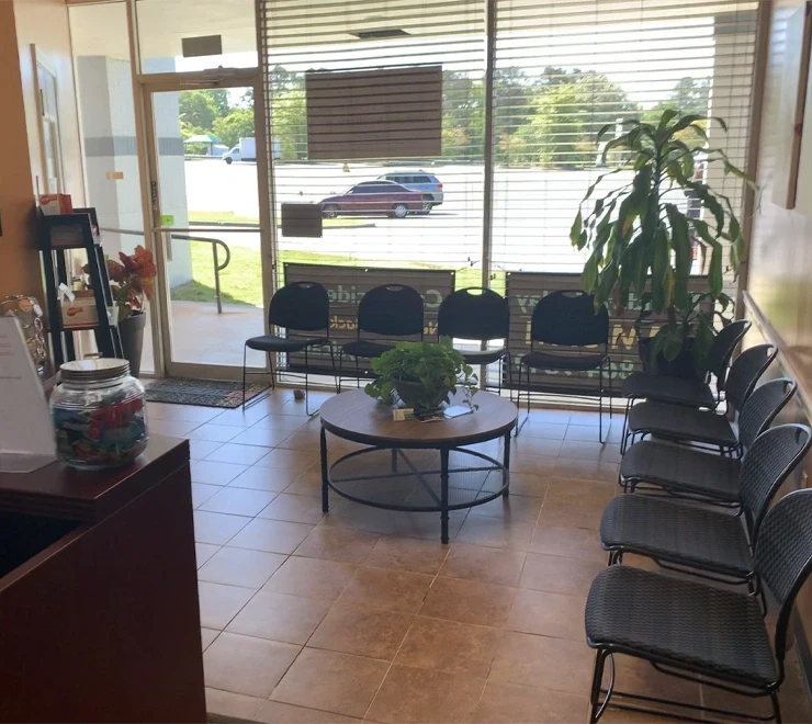 A waiting room with chairs lined along two walls, a round table with plants in the center